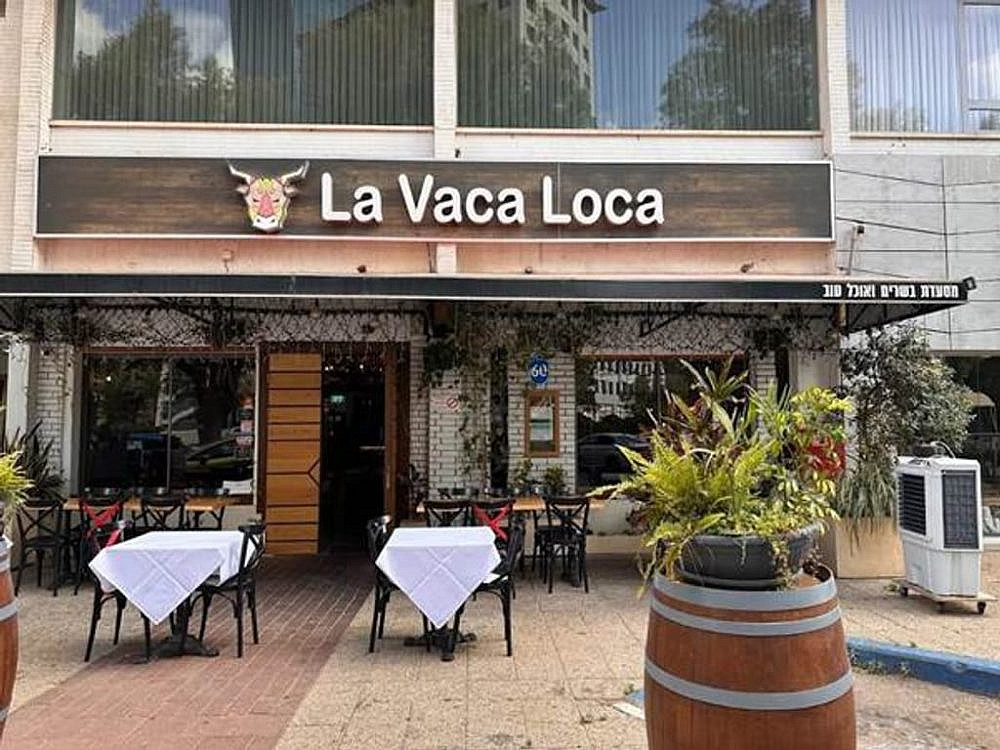 חזית מסעדת בשרים ארגנטינאית בהרצליה עם שלט La Vaca Loca ושולחנות ערוכים מחוץ למסעדה. צילום: לה ואקה לוקה